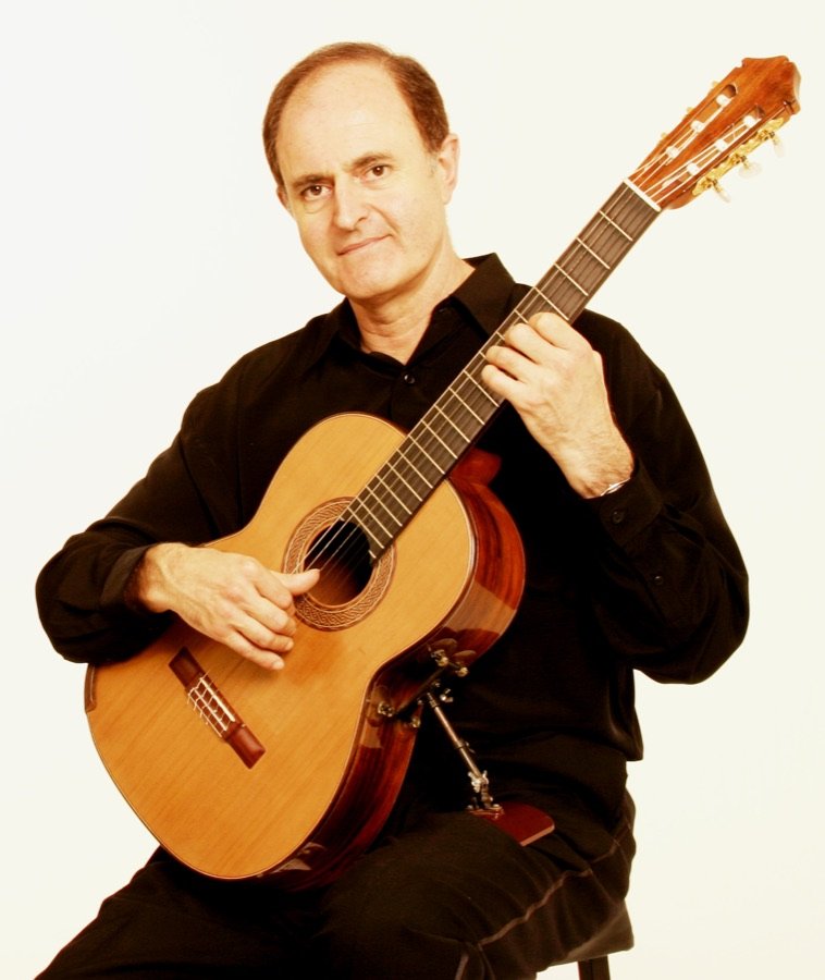 Julian Byzantine seated, playing guitar, against a white background